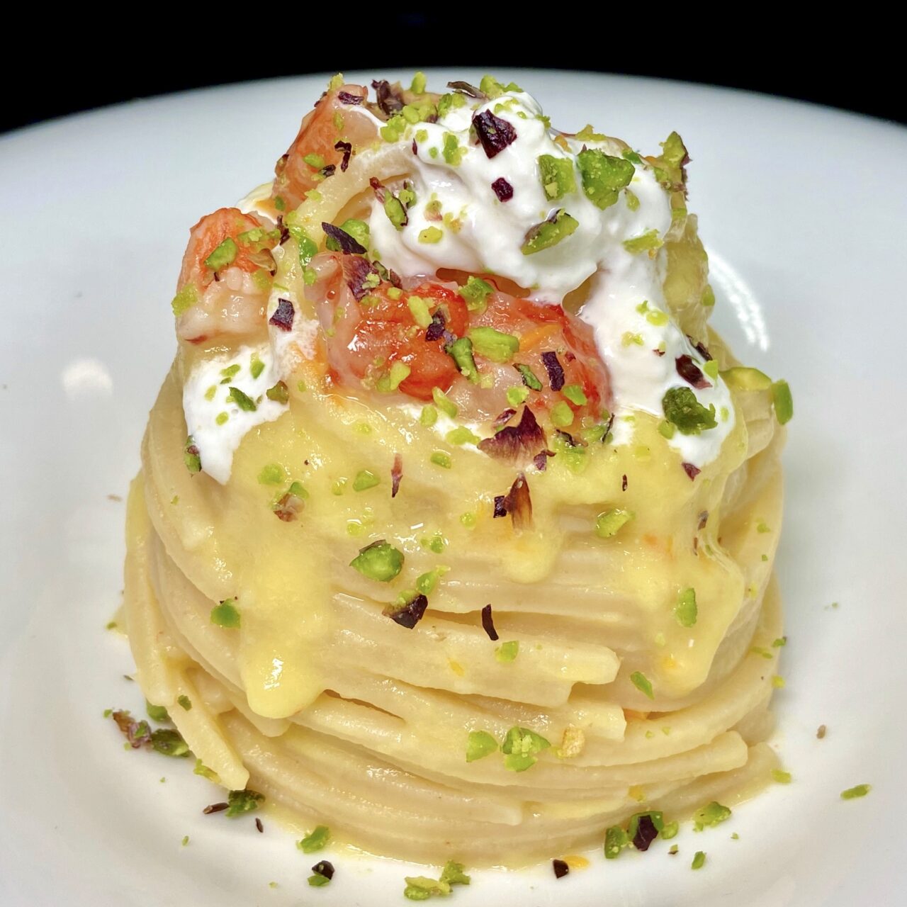 Chitarra mit gelben Datterini-Tomaten, Garnelen, Burrata-Käse und Pistazien.