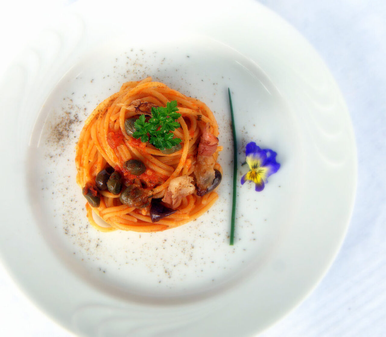 Spaghetti al pomodoro con guanciale croccante, olive taggiasche e capperi
